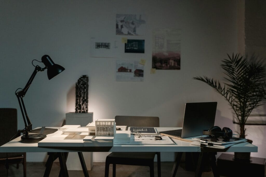 A contemporary architect's desk with design plans, laptop, and lamp in a spacious office.